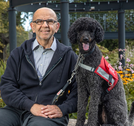 person with black poodle in red vest